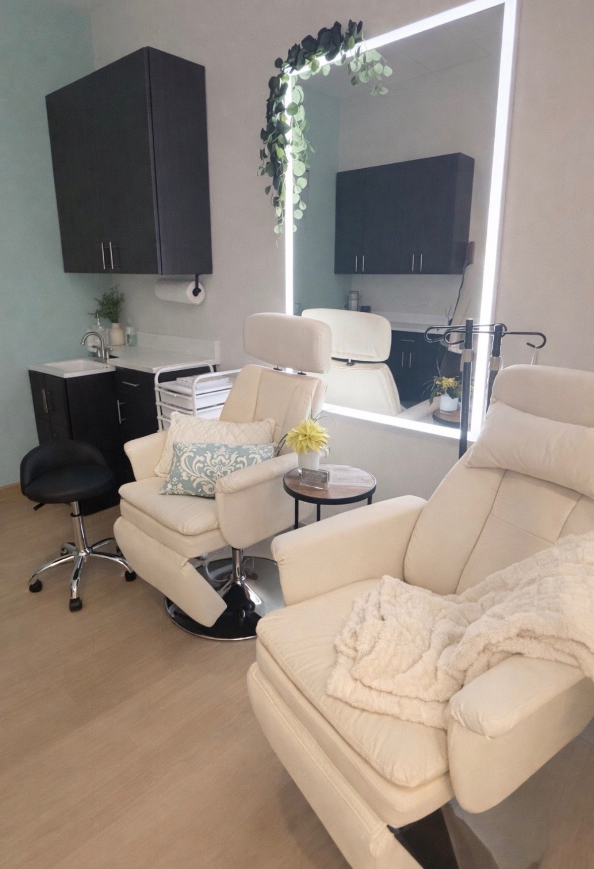 Cream treatment chairs beneath a softly lit mirror with eucalyptus
